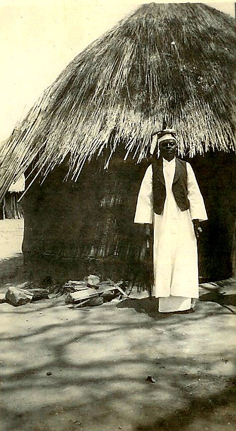 Chief Kakumbi standing before a thatched house at his village
